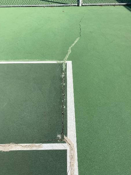Crack running through court line intersection with crumbling surface material at Camino Real Park