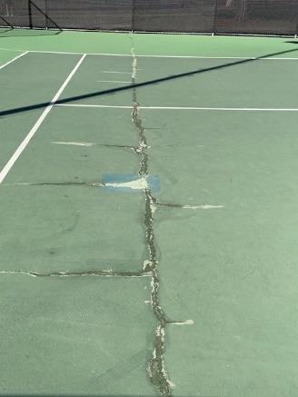 Large crack running across a Camino Real Park tennis court with failed patch repairs visible
